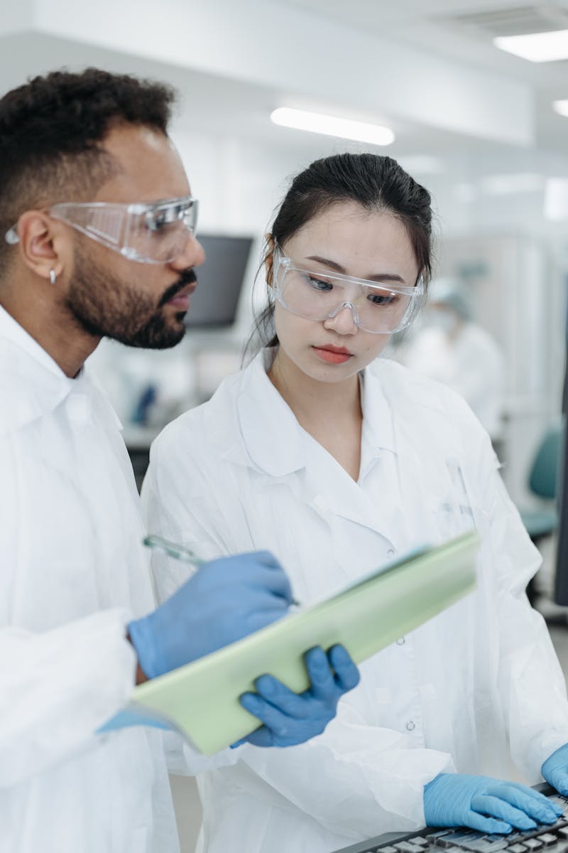 Two scientists in protective gear reviewing notes in a modern laboratory setting.